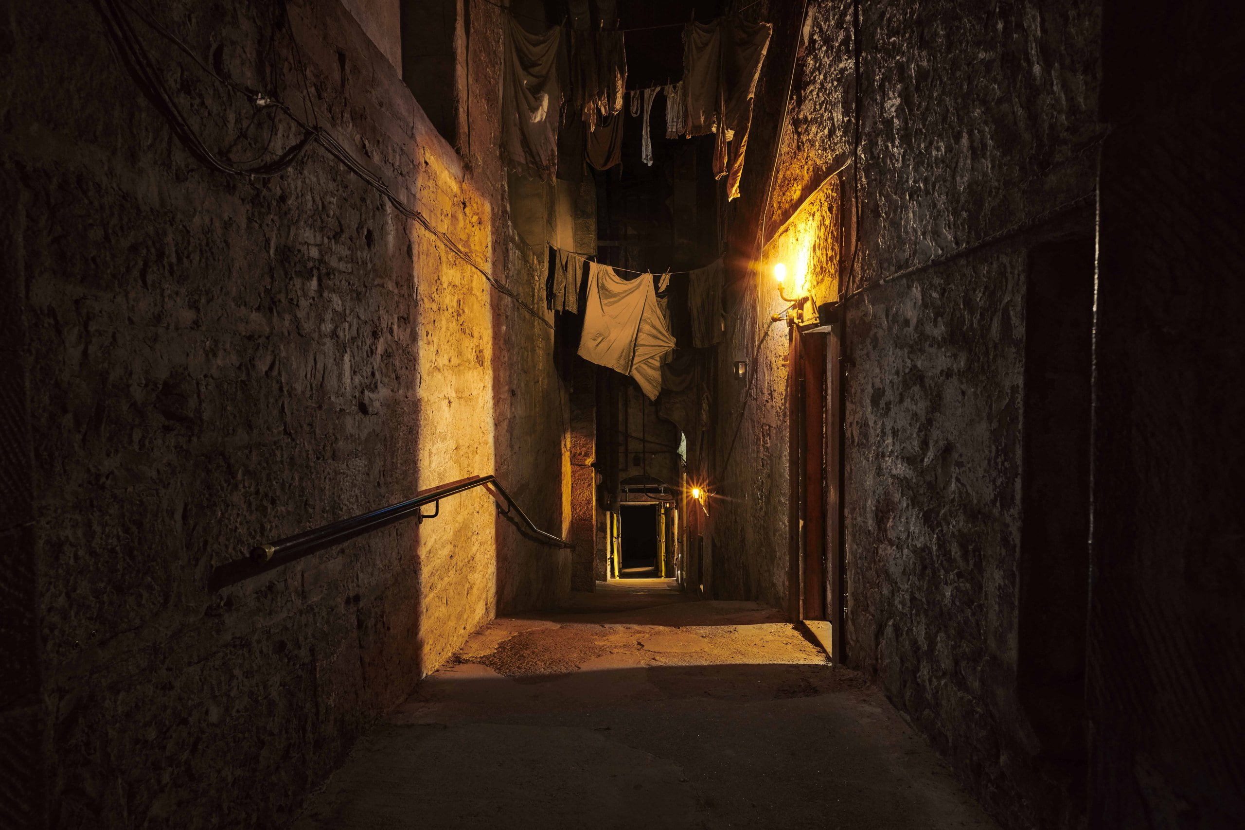 Mary King's Close - a narrow stone alleyway with steps. It is dark outside and light comes from the doorways. Clothes are hanging up to dry on lines between the buildings.